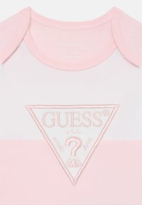 Bodysuit de bebé de manga curta em branco e rosa claro. Apresenta um logótipo bordado num patch triangular ao centro. Feito em algodão orgânico.