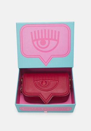 Rode leren clutch met reliëf oogdesign in een blauwe en roze doos met hetzelfde oogmotief op de deksel en de bodem.