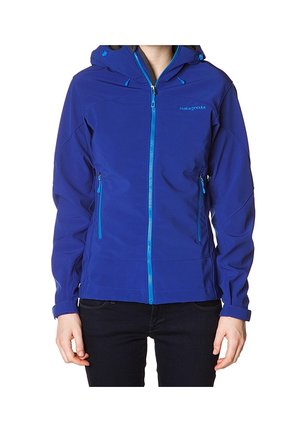 Personne portant une veste à capuche bleue zippée avec des poches latérales et des poignets ajustables, debout sur un fond blanc.