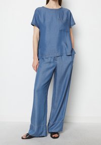 Completo in denim composto da un top a maniche corte con tasca sul petto e pantaloni a gamba larga, entrambi in azzurro chiaro, con dettagli di cucitura ben visibili.