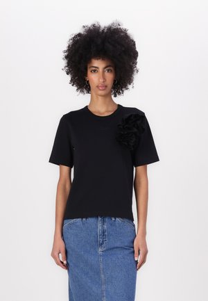 Black t-shirt with short sleeves, featuring a textured synthetic flower accent on the left shoulder and a crew neck design.