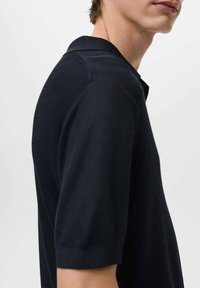 Polo azul marino con un diseño de punto texturizado, un cuello clásico y mangas cortas. La tela tiene un acabado suave con un ribete sutil.