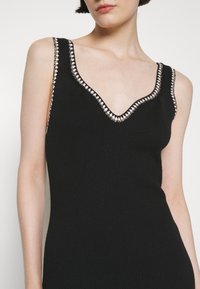 Robe débardeur noire côtelée avec un décolleté en V profond et une bordure en perles contrastantes le long de l'encolure. Design ajusté, tissu texturé.