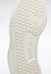 Biała gumowa podeszwa buta z wzorem diamentowym, z zaokrąglonym wzorem w kształcie okręgu i wytłoczonym logo "Reebok".