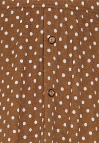 Bruine stof met witte stippen, met een verticale rij knopen van een bruin houtachtig materiaal en twee zichtbare knopen.