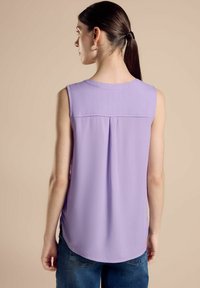 Top senza maniche di un delicato colore lavanda, con scollatura rotonda, caratterizzato da una piega sul retro e un orlo curvo, abbinato a jeans blu.