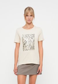 Beige bomull t-skjorte med et metallisk leopardmønster i kvadratisk design i midten. Korte ermer og rund hals, kombinert med et rutete skjørt.