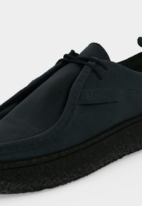 Chaussure décontractée en daim noir avec lacets à l'avant, semelle épaisse texturée et logo "SAMSOE" sur le panneau latéral.