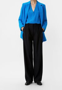 Blazer leggero e blu brillante sopra un top blu scuro; abbinato a pantaloni neri a palazzo a vita alta. Le scarpe nere completano l'outfit.