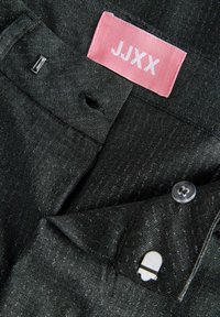 Melnas džinsa bikses ar rozā etiķeti ar uzrakstu "JJXX", priekšpusē ar pogu aizdari un nelielu metāla akcentu jostasvietā.