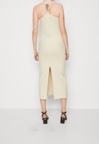 Beige pletené midi šaty s přiléhavým střihem, tenkými ramínky, vertikálním pruhovaným vzorem a rozparkem na zadní straně. V kombinaci s černými sandály na silném podpatku.