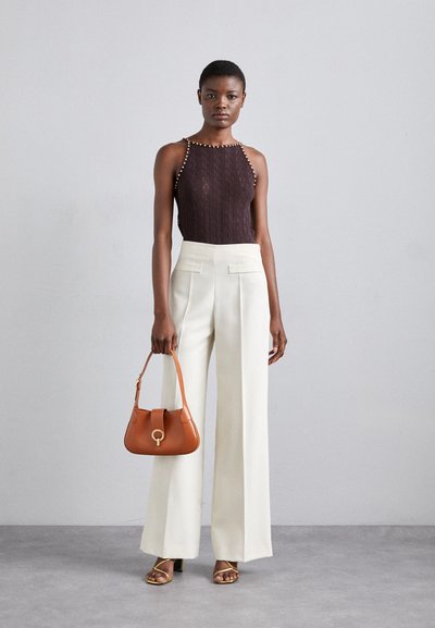 Brun strikket tanktopp med nagledekor, beige vid bukse, gullfargede heler med remmer og en liten oransje håndveske med sirkulært clasp.