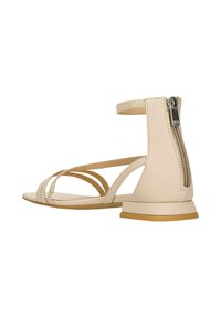 Sandale beige à lanières avec un petit talon carré, bout ouvert et fermeture zippée sur le côté. Caractérisée par plusieurs fines lanières et une finition en cuir lisse.