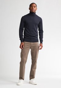 Maglione a dolcevita navy in morbido tessuto abbinato a pantaloni marrone chiaro e sneakers bianche, caratterizzato da un design aderente e polsini a costine.