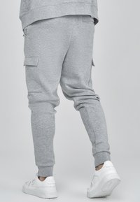 Graue Jogginghosen aus weichem Stoff, mit seitlichen Cargo-Taschen und schmaler Passform, kombiniert mit weißen Turnschuhen.