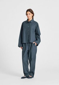 Camicia oversize di un blu scuro, con maniche lunghe, chiusura con bottoni e pantaloni larghi coordinati, entrambi realizzati in un tessuto morbido. Scarpe slip-on comode.