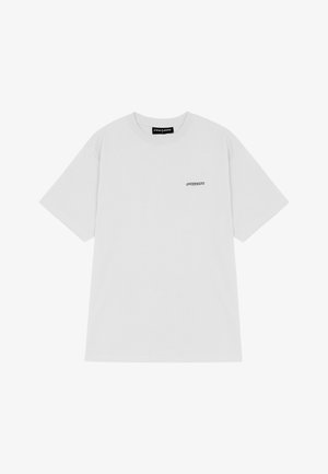 Balta medvilnė marškinėliai su apvaliu iškirpimu ir trumpomis rankovėmis. Ant kairiojo krūtinės pusės yra mažas juodas logotipas. Paprastas ir nepuošnus dizainas.