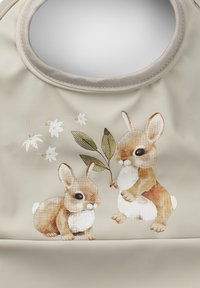 Beige tyg med en illustration av två kaniner; en håller ett blad och den andra sitter i närheten, omgiven av små vita blommor.