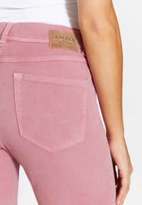 Růžové džínové kalhoty mají viditelnou zadní kapsu s jemným šitím a koženou visačkou označenou "ANGELS" na pasu.