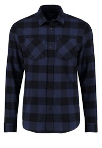 Chemise à manches longues à carreaux bleus et noirs, avec un devant boutonné, comportant deux poches poitrine, fabriquée en tissu doux avec une texture lisse.