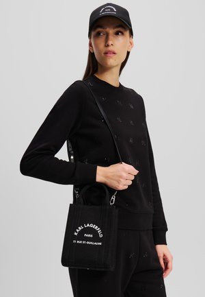 Sudadera negra de algodón con logo texturizado, combinada con un pequeño bolso estructurado negro que presenta texto impreso en blanco y detalles de hardware plateado.