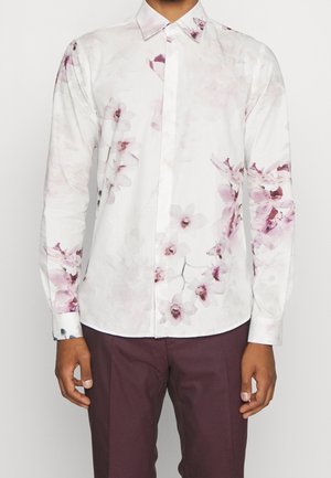 White long-sleeve button-up shirt with light pink and purple floral print, worn with dark purple pants, shown from neck to hips.