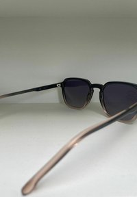 Occhiali da sole neri e rosa gold con montatura quadrata e lenti scure. Le astine presentano una sfumatura morbida dal nero al rosa gold.