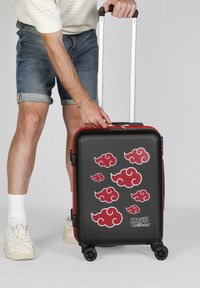 Maleta rígida negra con diseños de nubes rojas, mango retráctil y cuatro ruedas; presenta un logo que dice "Naruto Shippuden."