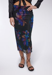Gonna nera floreale con motivo floreale astratto e colorato; tessuto morbido e leggero; lunghezza al ginocchio; abbinata a sandali neri con cinturini.