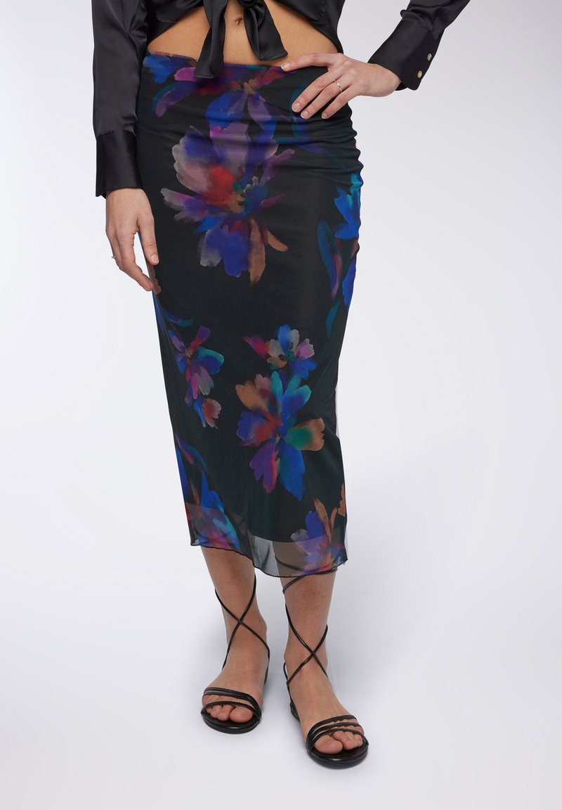 Gonna nera floreale con motivo floreale astratto e colorato; tessuto morbido e leggero; lunghezza al ginocchio; abbinata a sandali neri con cinturini.