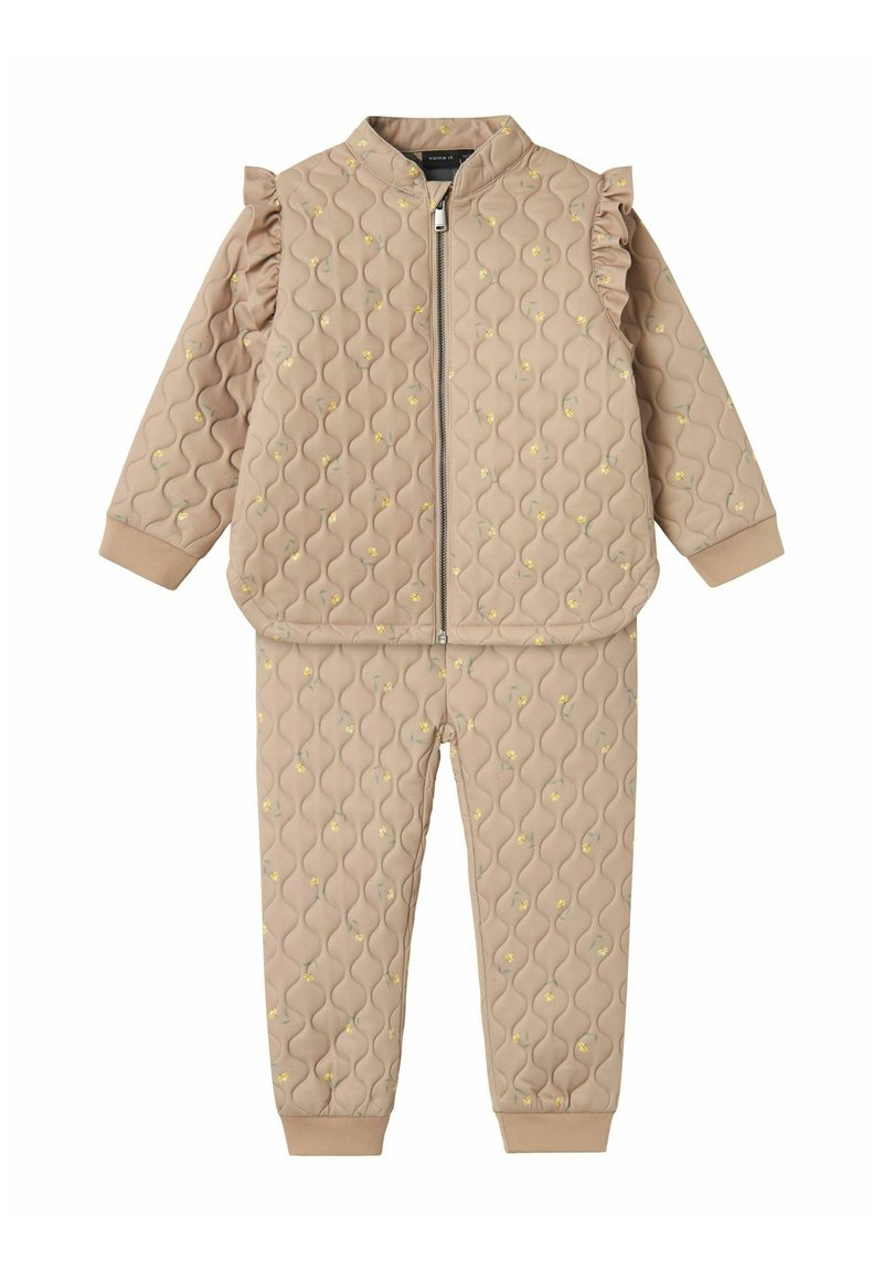 Quilted beige jakke og bukser med flæser på skuldrene og blomsterprint, featuring en lynlåslukning og elastiske manchetter ved håndled og ankler.