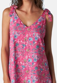 Abito senza maniche rosa con scollo a V e spalline legate, caratterizzato da un motivo floreale in blu, viola e verde, realizzato in tessuto leggero.