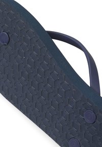 Navy modré gumové žabky se spodní částí s texturovaným hexagonálním vzorem. Tenký pásek a zakulacený podpatek, dvě kulaté knoflíky blízko spodní části.