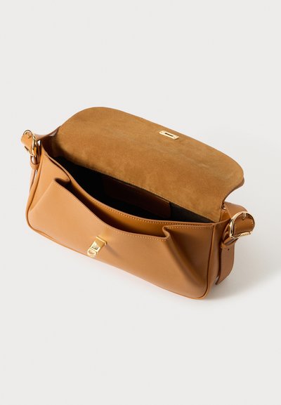 Tan leren schoudertas met een suède flap, gouden hardware en een ruime binnenkant. De buitenkant is glad met zachte randen.