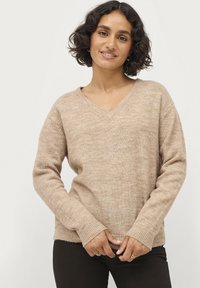 Beige v-hals trui met een gestructureerd breipatroon. Bevat ribbels aan de mouwen en onderrand, met een ontspannen pasvorm die iets voorbij de taille reikt.