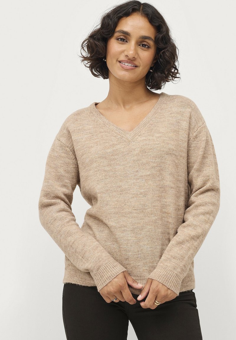 Beige v-hals trui met een gestructureerd breipatroon. Bevat ribbels aan de mouwen en onderrand, met een ontspannen pasvorm die iets voorbij de taille reikt.