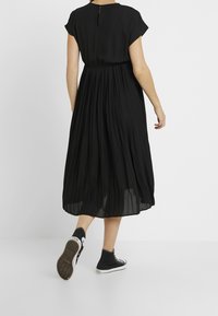 Mustapleated-mekko, jossa on hihattomat hihat ja avainaukko selässä. Yhdistetty mustiin korkeakantaiseen lenkkariin. Pehmeä kangas, virtaava muotoilu.