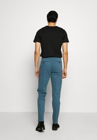 Zwart heren t-shirt gecombineerd met slim-fit, lichtblauwe chino's. De chino's hebben achterzakken met knoopsluitingen. Model draagt zwarte laarzen.
