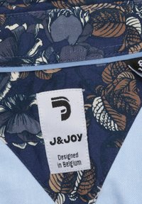 Marine stof met een bloemenpatroon in aardetinten, met een wit label dat "J&Joy" en "Ontworpen in België" toont. Textuur ontwerp.