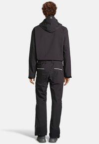 Giacca nera da esterno con cappuccio e polsini regolabili, abbinata a pantaloni neri coordinati con tasche con zip e design a gamba dritta.