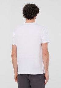 Biała bawełniana koszulka z krótkim rękawem, okrągłym dekoltem i prostym wzorem. Materiał wydaje się być miękki i lekko teksturowany.