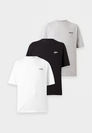 Zwei Personen stehen nebeneinander und tragen passende graue übergroße T-Shirts und lockere dunkle Hosen mit weißen Sneakers vor einem einfarbigen weißen Hintergrund.