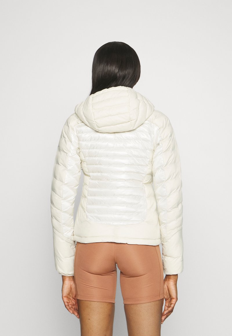 Chaqueta blanca acolchada con capucha. Presenta una combinación de acabados brillantes y mate, textura acolchada y una silueta ajustada.