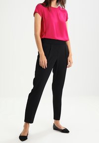 Blusa fucsia de manga corta combinada con pantalones negros ajustados. Los pantalones presentan un diseño plisado y un corte slim; se llevan con zapatos planos negros.