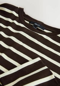 Hnedo-krémové horizontálne pruhované tričko s dlhým rukávom, okrúhlym výstrihom a viditeľnou značkovou štítkom „NEXT“ na golieri.