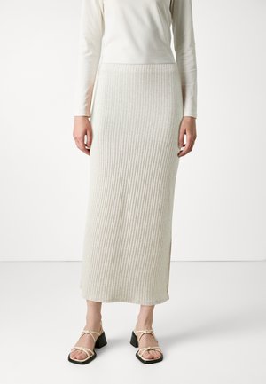 Ribbed, beige knit skirt with a fitted waist and side slits. Paired with strappy black sandals featuring a square toe and block heel.