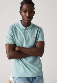 Light blue polo shirt with a collar, three button placket, and small red Levi's logo on the chest. Worn with light denim jeans.