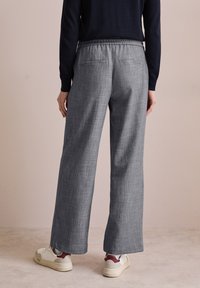 Pantaloni grigi a gamba larga con finitura testurizzata e vita elastica. Sono visibili le tasche posteriori. Abbinati a sneaker bianche e una maglietta blu navy.