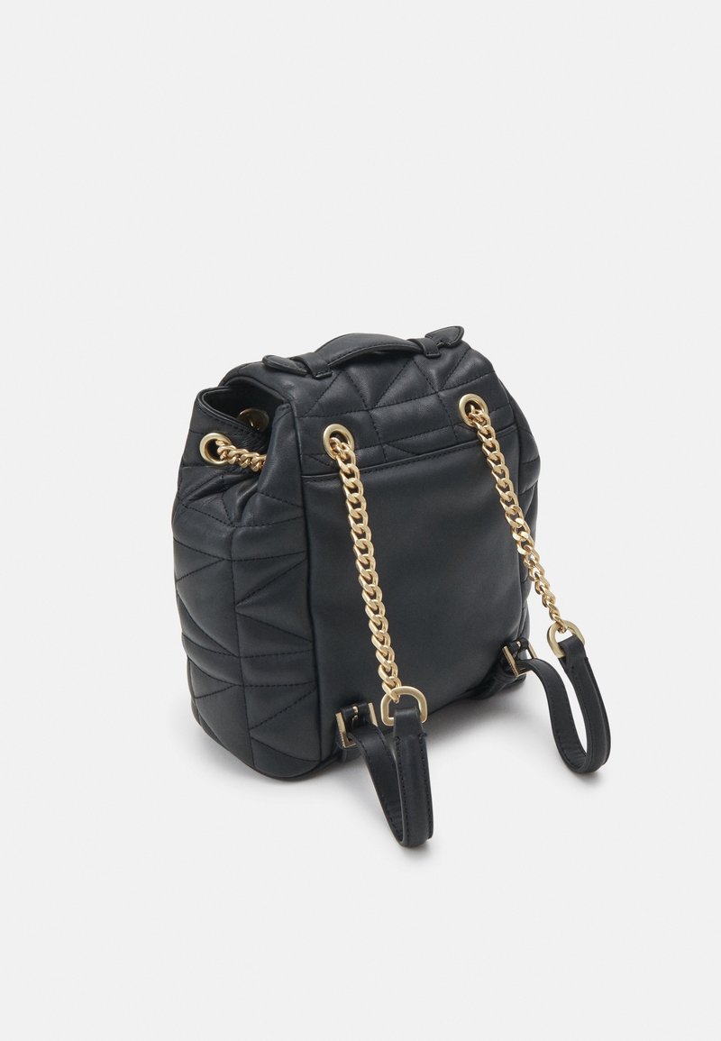 Sac à dos en cuir noir matelassé avec des bretelles en chaîne dorée et des poignées en cuir noir sur fond blanc.