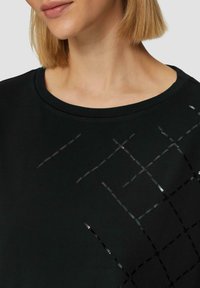 Zwarte sweatshirt met een ronde halslijn, voorzien van een gestructureerd ontwerp van elkaar kruisende glanzende zwarte lijnen die een gridpatroon op de voorkant vormen.